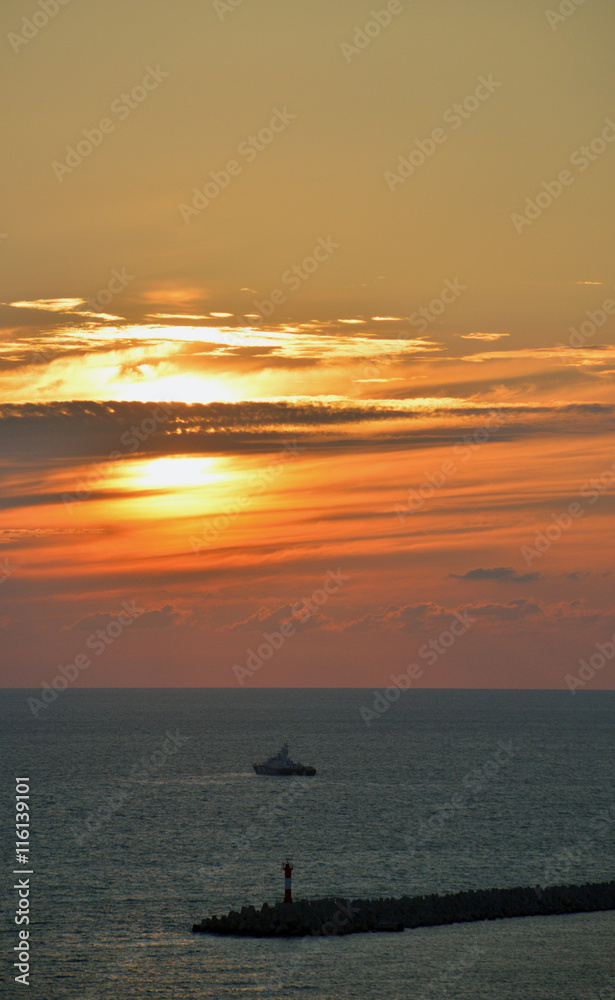 Маяк морского порта и корабль на фоне заходящего солнца 