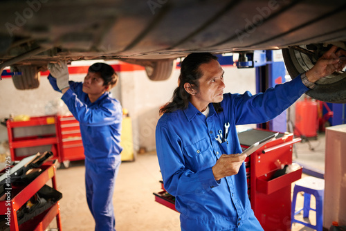 Team of professional mechanics examining car in garage
