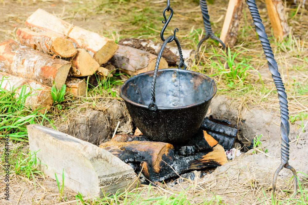 Empty outdoor cooking pot hanging over burnt wood and ashes. Pot is handmade blackened iron with rivets. Empty outdoor cooking pot hanging over burnt wood and ashes. Pot is handmade blackened iron with rivets.