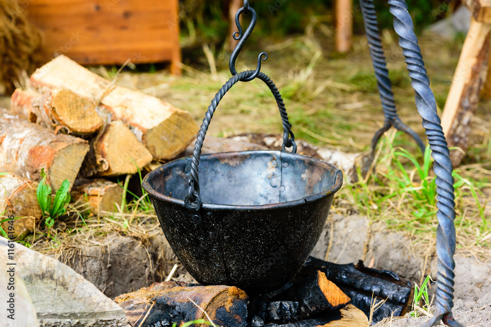 Empty outdoor cooking pot hanging over burnt wood and ashes. Pot is handmade blackened iron with rivets. Empty outdoor cooking pot hanging over burnt wood and ashes. Pot is handmade blackened iron with rivets.