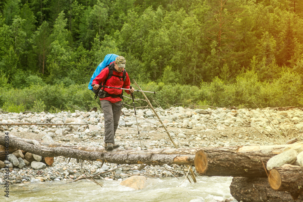 Man hiker walking across river in a forest Man hiker walking across river in a forest