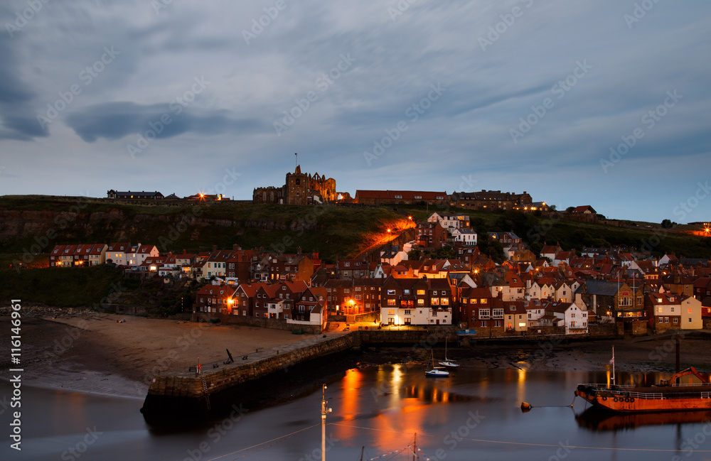 WHITBY, ENGLAND - JULY 16: The ruins of Whitby Abbey, with the harbour in the foreground, at dusk. In Whitby, North Yorkshire, England. On 16th July 2016.