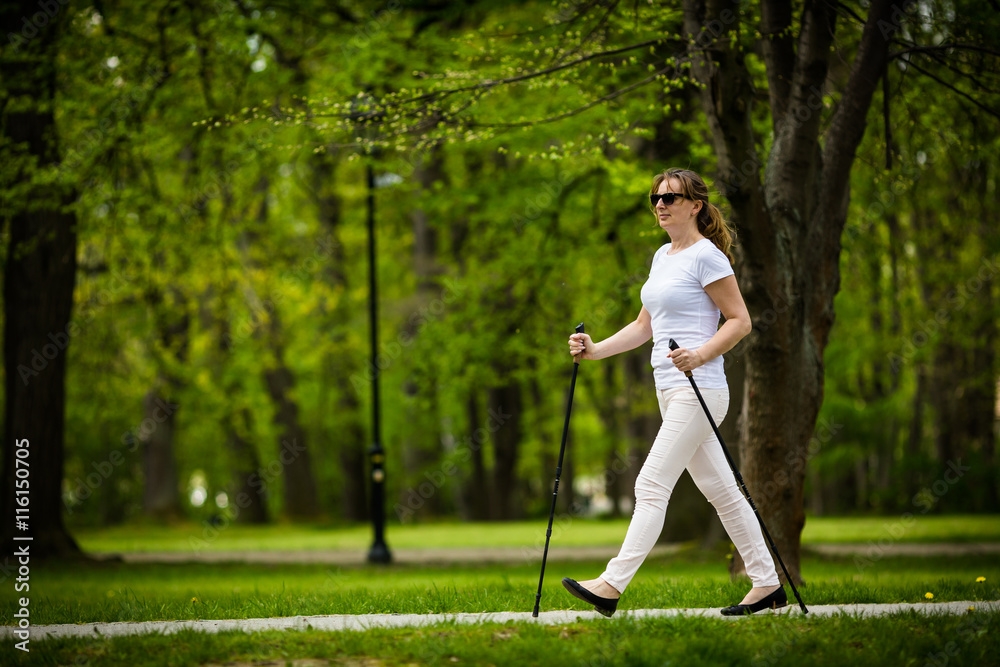 Nordic walking - middle-age woman working out in city park 