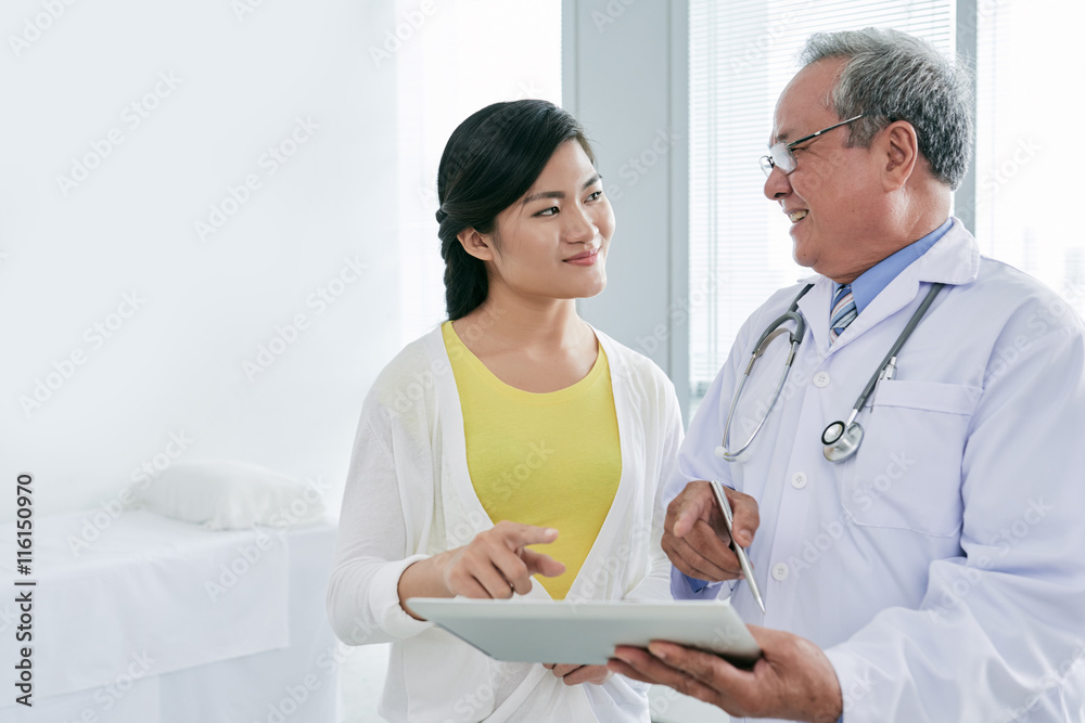 Pretty young woman with tablet computer consulting her doctor Pretty young woman with tablet computer consulting her doctor