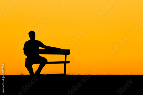 A silhouette of man sitting on bench in sunset