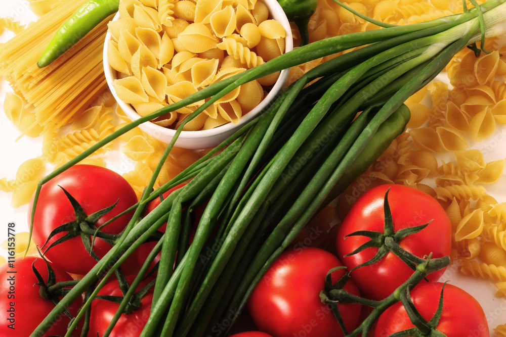 Different types of raw Italian pasta with tomatoes and other vegetables. Top view background.