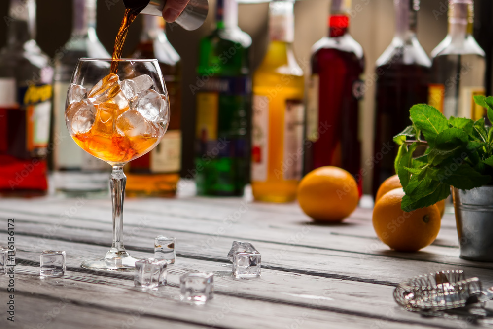 Jigger pours liquid into wineglass. Mint and oranges. Beverage being prepared at club. Imported rum of high quality. Jigger pours liquid into wineglass. Mint and oranges. Beverage being prepared at club. Imported rum of high quality.