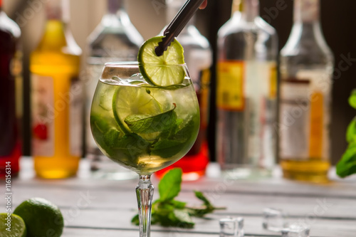 Tongs holding slice of lime. Beverage with leaves of mint. Hugo cocktail made by bartender. Relax and have a drink.