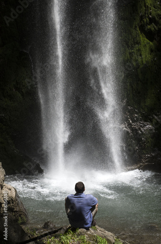 Man sitting in front of the spray of a waterfall
