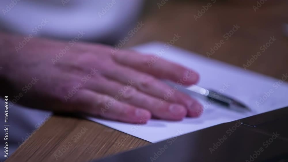 A man is having his hand on the papers in front of the computer and he is moving them to the left and pointing at something on the screen. Close-up shot.
