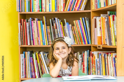 indoor portrait of young happy smiling girl reading book in libr