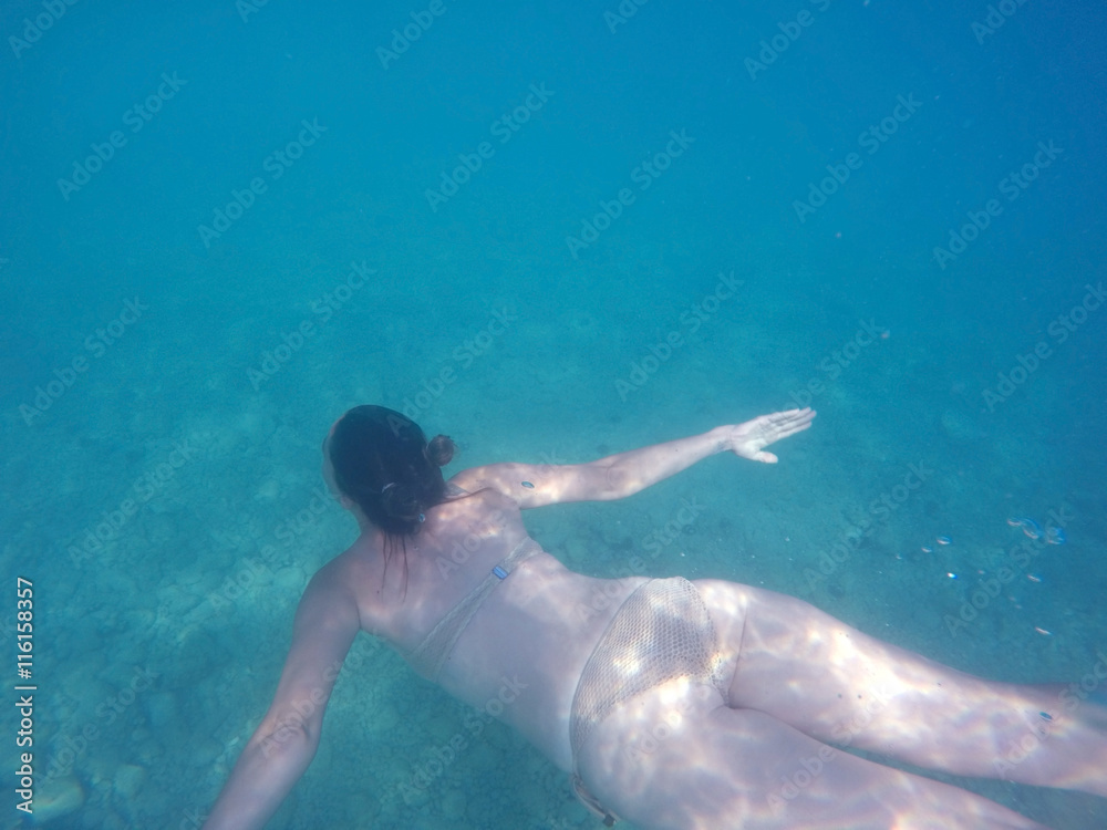 Young girl in bikini diving in blue clear sea top view