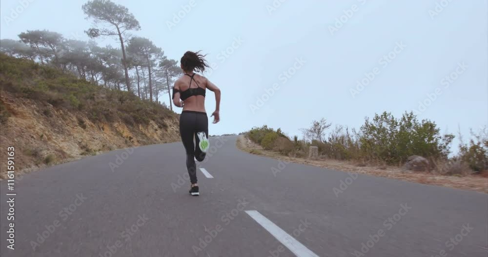 Young female athlete in sportswear taking break from running on the road in morning. Fitness woman in sportwear during outdoor running session.
