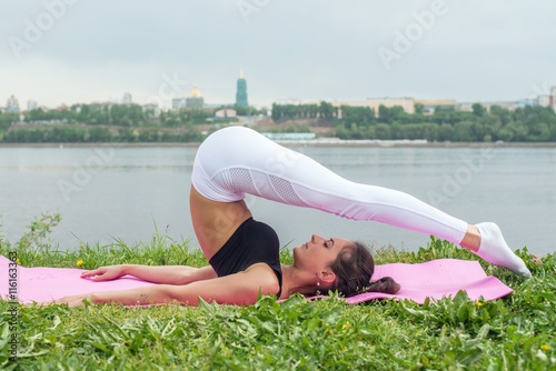 Fit woman making yoga in plow pose on mat in nature photo