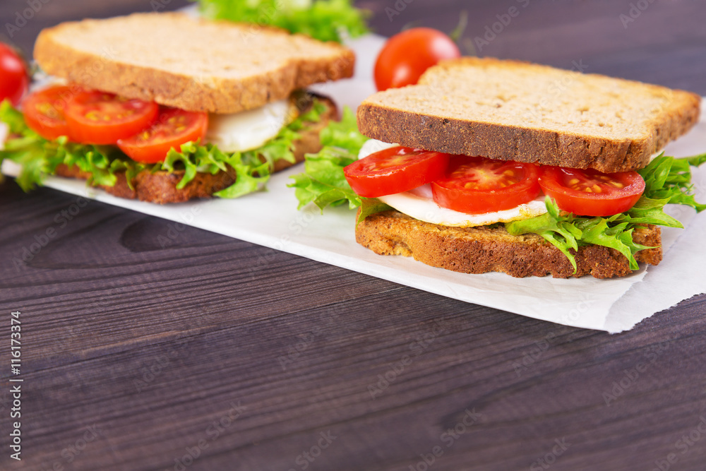Two homemade sandwich with egg, salad and tomatoes on crispy slice of rye bread on a dark wooden background Two homemade sandwich with egg, salad and tomatoes on crispy slice of rye bread on a dark wooden background