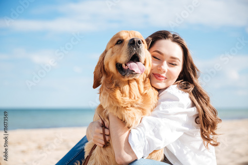 Canvas Print Tender smiling young woman hugging her dog on the beach