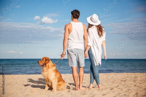 Back view of couple walking with dog on the beach photo