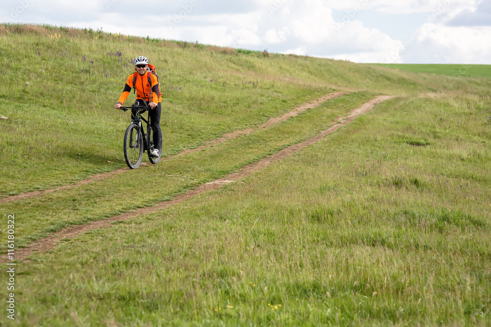 Obraz premium Young man cycling on a rural road through green meadow