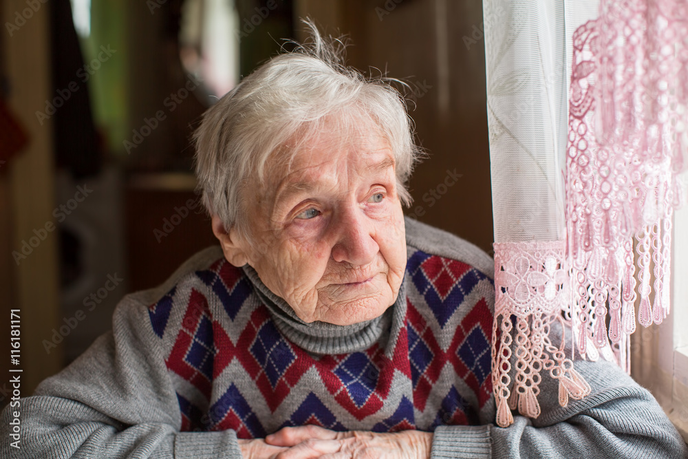 Elderly woman in a sweater looking out the window sitting at the table. Elderly woman in a sweater looking out the window sitting at the table.