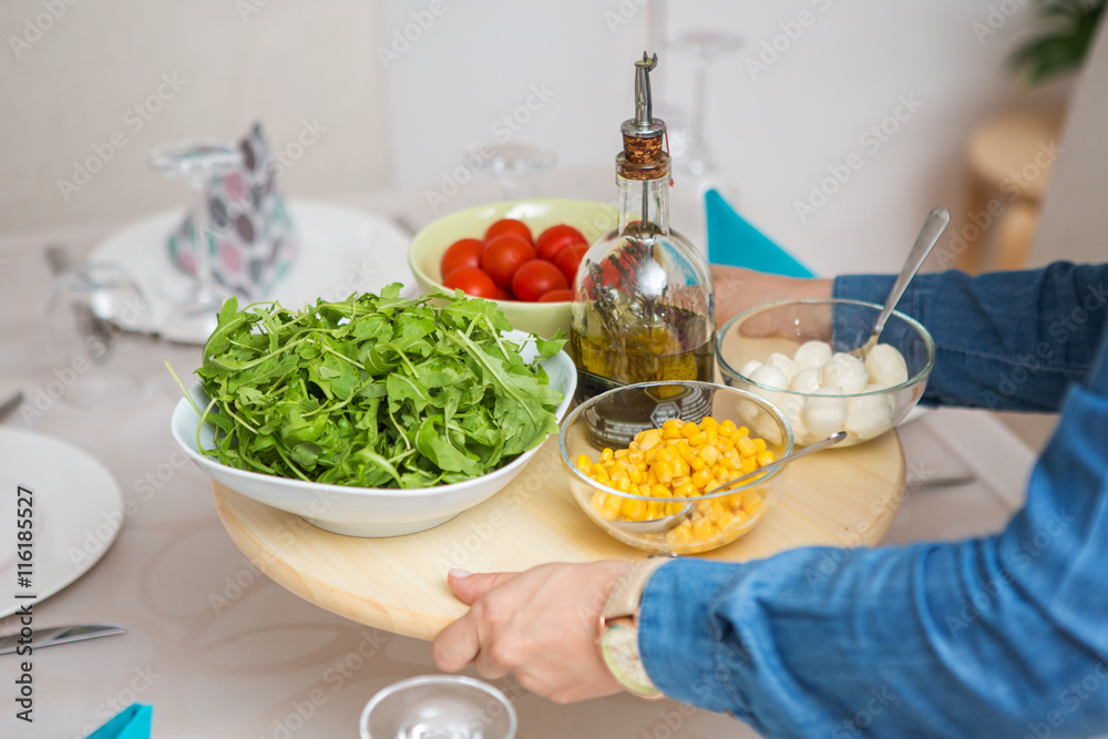 Woman bringing a wooden tray with fresh organic arugula, tomato Woman bringing a wooden tray with fresh organic arugula, tomato