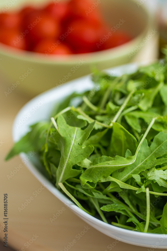 Fresh organic arrugula tossed in a white bowl, unseasoned, with Fresh organic arrugula tossed in a white bowl, unseasoned, with