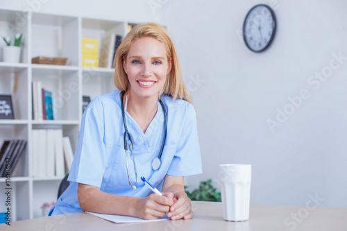 Beautiful blonde female doctor sitting at office desk working. Health care and prevention concept