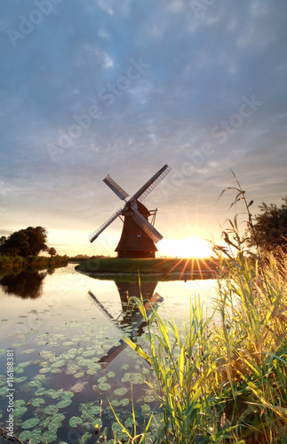 gold sunshine behind Dutch windmill by river