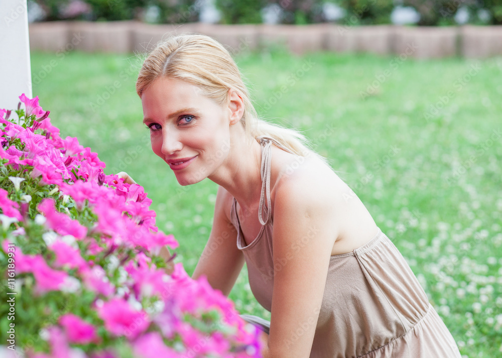 Beautiful blonde young woman smells flowers in a garden Beautiful blonde young woman smells flowers in a garden