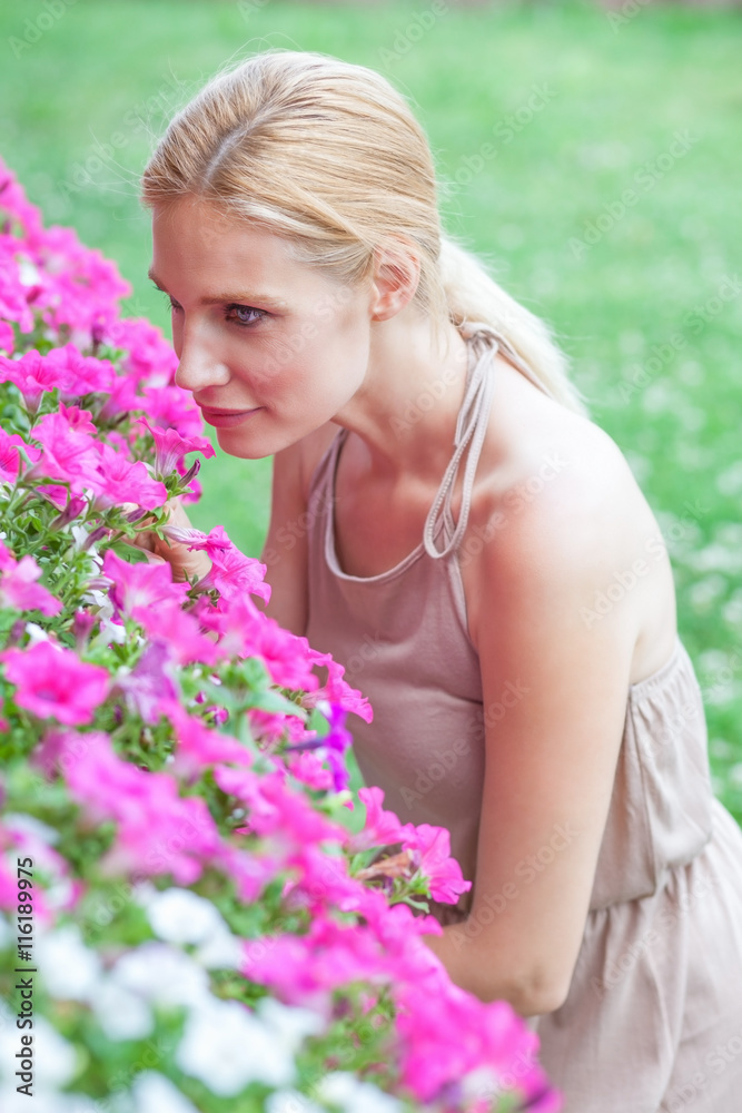 Fototapeta premium Beautiful blonde young woman smells flowers in a garden