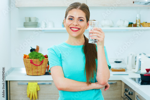 Smiling woman standing in kitchen holding water glass.