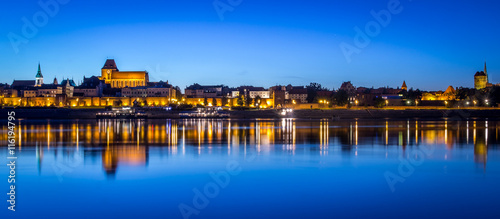 Panoramic view of Torun Old Town at night reflected in Vistula river, Poland