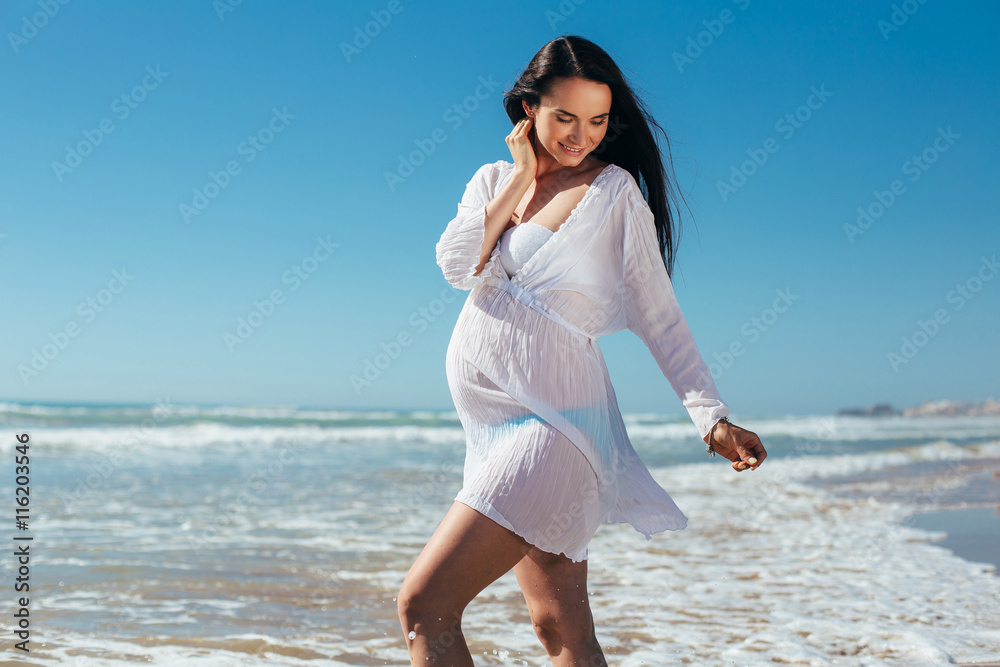 Young happy pregnant woman relaxing and enjoying life in nature. Outdoor shot. Beautiful pregnant woman standing on the beach. Young happy pregnant woman relaxing and enjoying life in nature. Outdoor shot. Beautiful pregnant woman standing on the beach.