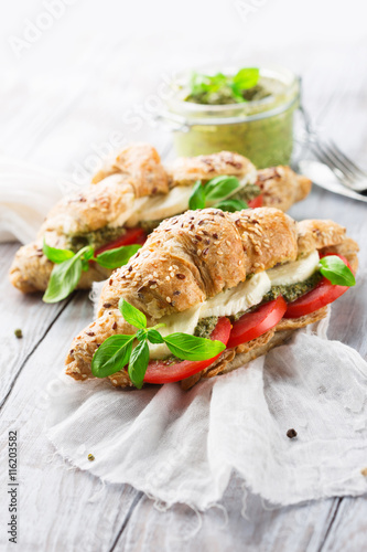 Crunchy wholegrain croissants with mozzarella, tomato and homemade pesto sauce on rustic white wooden background, selective focus