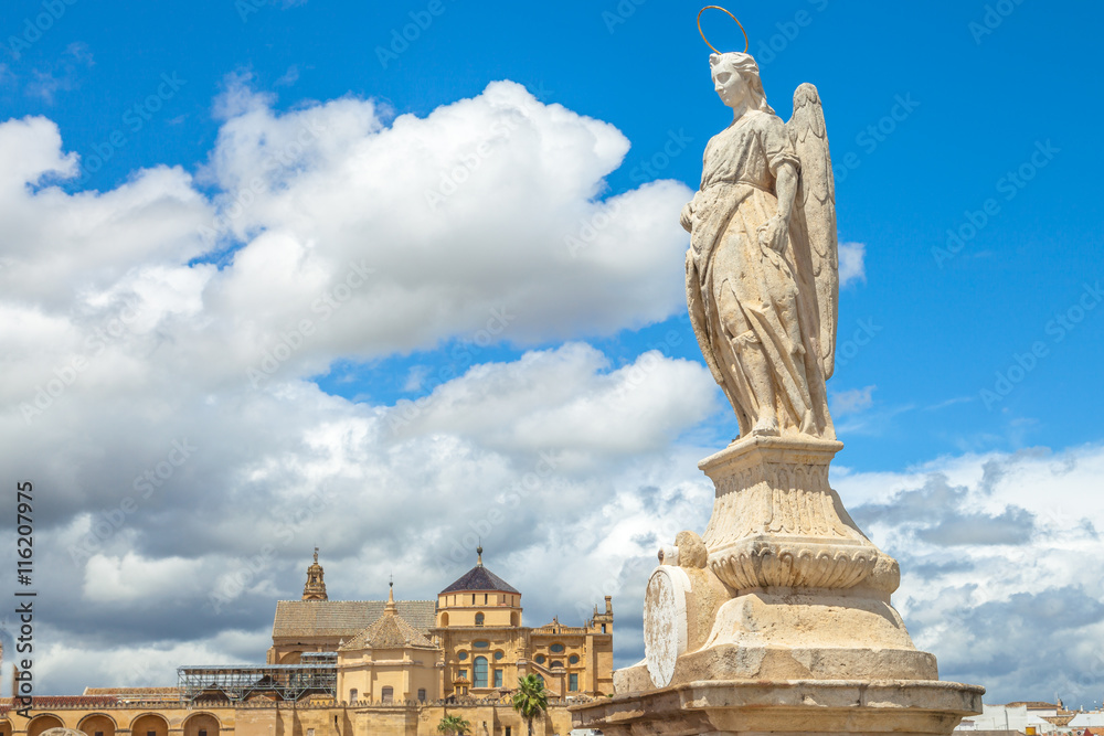 San Rafael Archangel statue on the popular Roman Bridge in Cordoba with behind the Cathedral of the Andalusian city, Spain.