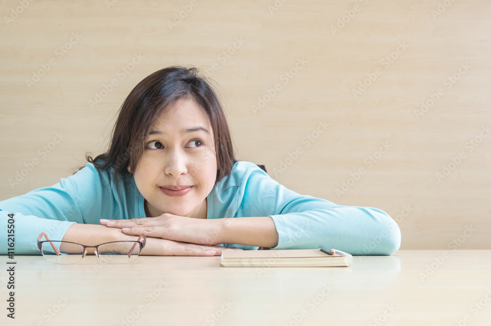 Closeup asian woman lied on desk with happy face in rest time from reading a book on blurred wooden desk and wall textured background in the meeting room , happy time and relaxation of woman concept Closeup asian woman lied on desk with happy face in rest time from reading a book on blurred wooden desk and wall textured background in the meeting room , happy time and relaxation of woman concept