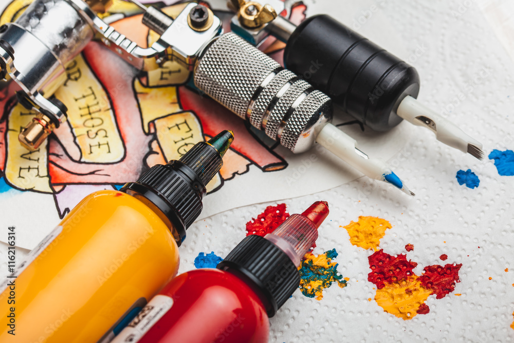 Replacement supplies for tattoo in sterile packages, sketches, inks and a tattoo machine on the white background of old boards