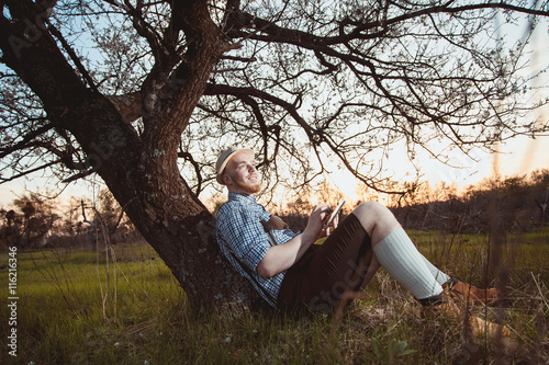 The theme is Oktoberfest, a guy in a beautiful mountain area lies in nature and looks at the tablet