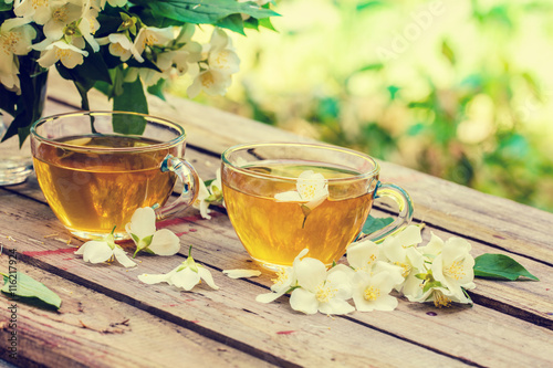 Two cups of green tea with jasmine flowers on grunge wooden table in the garden