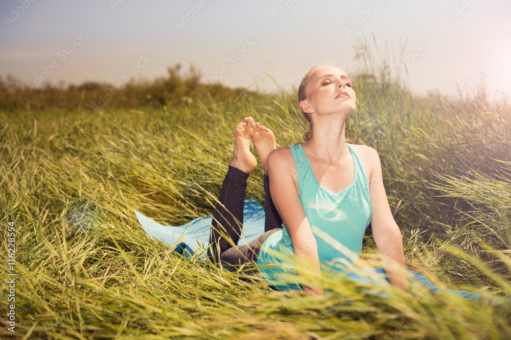 Fototapeta premium Young blond pretty woman doing yoga exercises on the grass