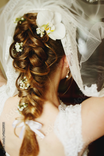 Bride puts on a veil above hair dressed in flowers