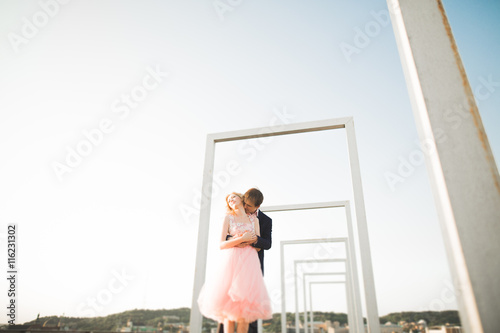 Young couple in love posing on roof with perfect city view holding hands and hugging . Beautiful sunset