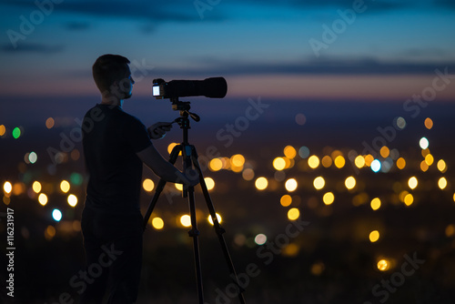 The man work with a camera on the background of night city light. Wide angle