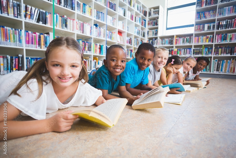 Smiling school kids lying on floor reading book in library Stock Photo ...