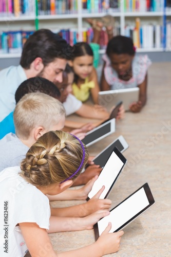 Teacher and kids lying on floor using digital tablet in library