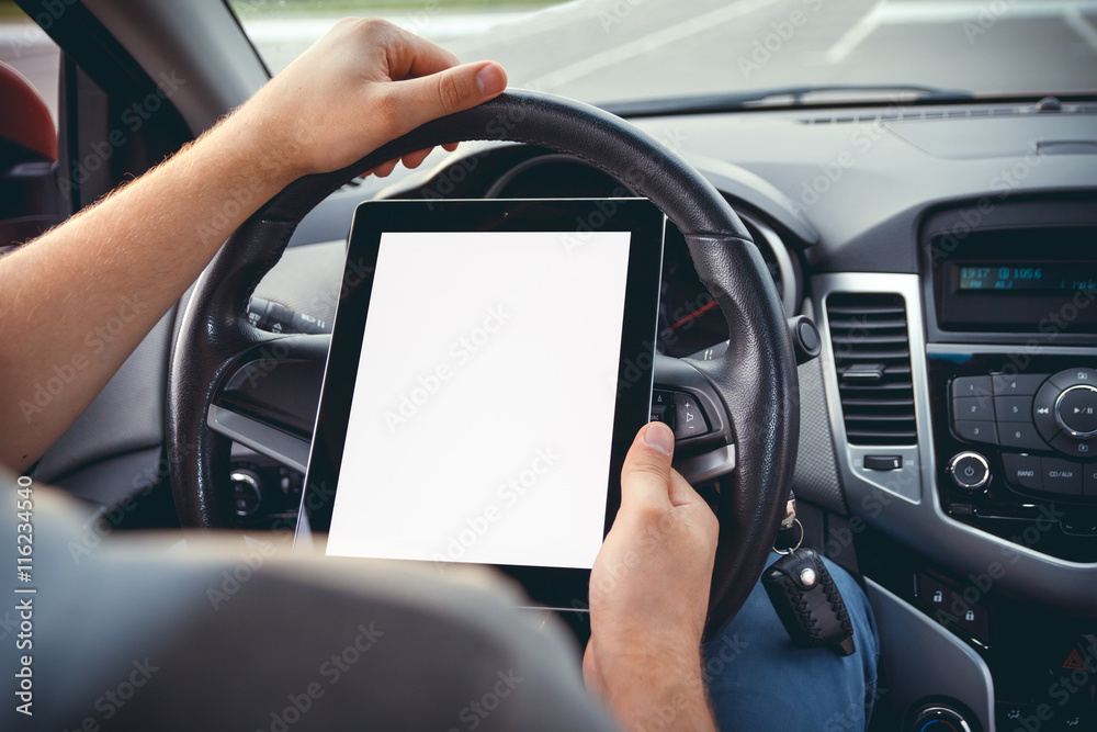 A young man with a tablet in his hand at the wheel of the car. Multitasking. Safe driving concep A young man with a tablet in his hand at the wheel of the car. Multitasking. Safe driving concep