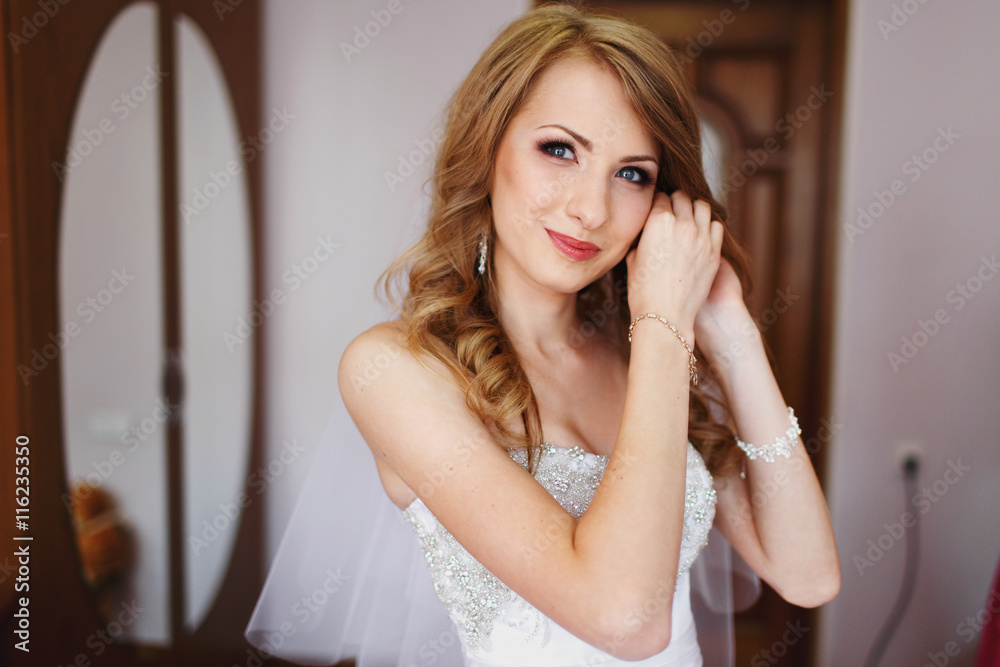 Fototapeta premium Bride smiles tender while putting on jewerly