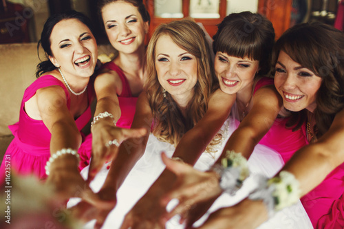 Bride and bridesmaids reach their hands out and smile