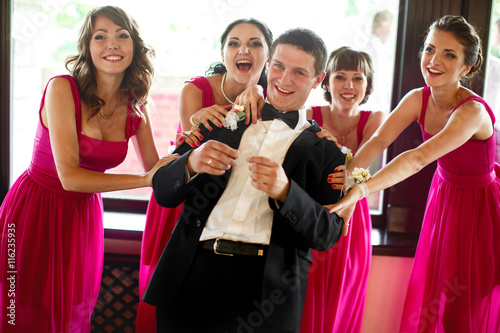Bridesmaids hold groom's shoulder and smile