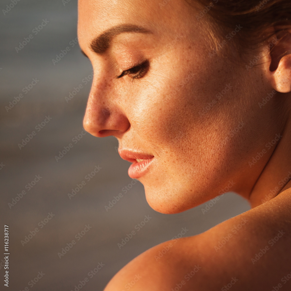 Naklejka premium portrait of beautiful young woman with freckles standing on the beach background 