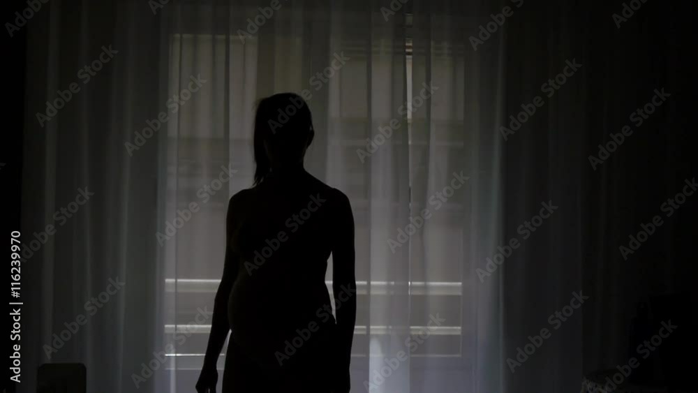 Pregnant woman moves away from the window. Silhouette. Slowmo. Pregnant woman moves away from the window. Silhouette. Slowmo.